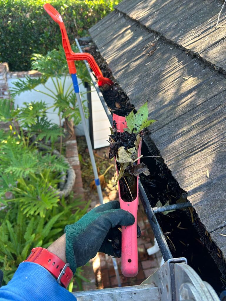 Technician using an extension tool to clean a gutter in San Diego