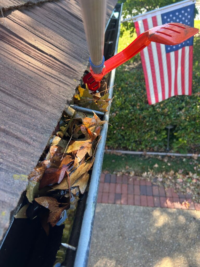 Gutter cleaning scoop clearing leaves along a wood shake roof
